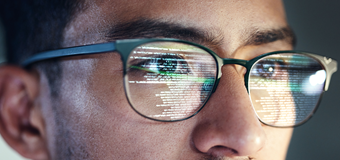 Tech worker coding with screen reflecting on glasses